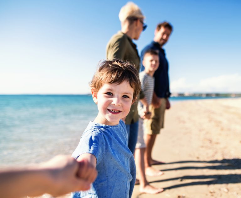 Young,family,with,two,small,children,standing,outdoors,on,beach.