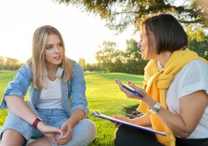 Conversation Of Young Woman With Psychologist, Social Worker, Outdoor At Meeting In Park On Lawn